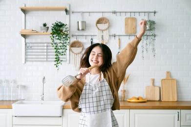 asian young woman dancing in kitchen room. she happy and relaxing at free time on weekend
