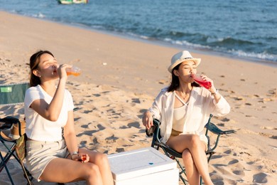 happy friends with drinks in camp and laughing together in holidays on sand beach near camping tent vacation time at sunset, young asian group woman and man in summer travel outdoor