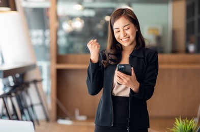excited happy asian woman looking at the phone screen, celebrating an online win, overjoyed young asian female screaming with joy, isolated over a white blur background