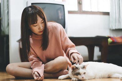 living with pet animal at home concept. young adult asian woman playing with lovely cat for friend when stay alone.