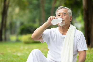senior man drinking water after workout or exercising in the park