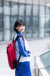 pretty chinese girl on campus, carrying a school bag with a cell phone to listen to music
