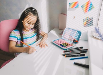 children, education and learning concept - schoolgirl writing at a desk at home.