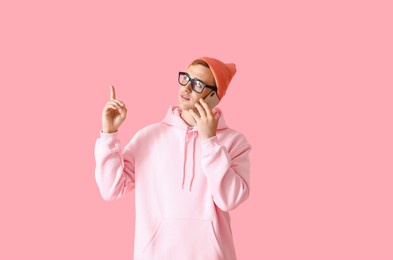 young guy in stylish hoodie talking by phone and pointing at something on color background