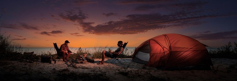 happy young friends resting by the bonfire near tent.