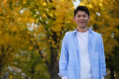 asian young man and blurred yellow ginkgo biloba tree in autumn. smiling at camera 