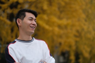 portrait of happy asian young man and blurred yellow ginkgo biloba tree in autumn. smiling side face