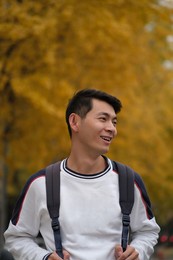 asian male college student and blurred yellow ginkgo biloba tree in autumn. carrying backpack  and smiling side face