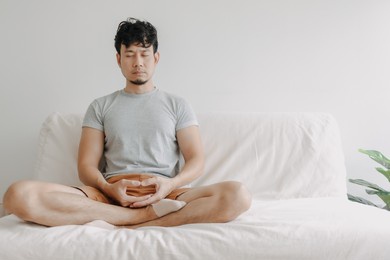 asian man do meditation on the sofa in his apartment. concept of wellbeing.