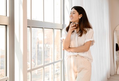 pretty young asian woman drinking tea near window