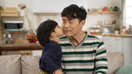 asian baby boy feeling shy after kissing dad on face in the living room at home. happy family concept
