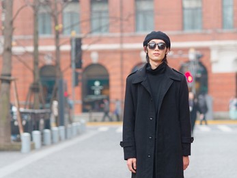 portrait of handsome chinese young man wearing black overcoat, sweater and trousers with sunglasses standing on shanghai street, front view, male fashion, cool asian young man lifestyle.