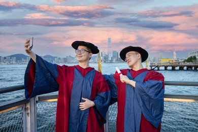 two happy proud phd graduated male students in academic dress gown selfie or take photo using mobile phone