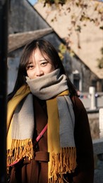beautiful asian girl in thick overcoat and with mouth covered in thick scarf smiling at camera. background is blurred asian vintage house and wall. 