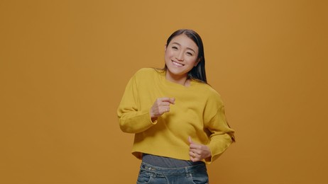 cheerful person doing celebratory dance moves on camera, enjoying movement to express happiness and entertainment. positive woman having fun with energic and joyful gesture in studio.