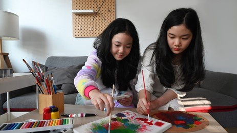 two cute asian girl painting picture on canvas with oil paints at home.