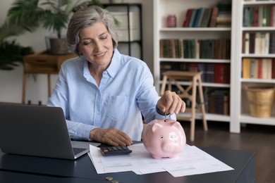 happy middle-aged woman put coin into piggybank, save money for future, make investment. provident economical female manage family finances, personal budget, expenses control. banking, economy concept