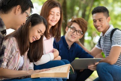 smiling schoolgirl reading a book surrounded by her classmates