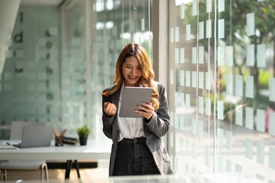 portrait attractive young asian business woman using digital tablet celebrate success or happy pose.