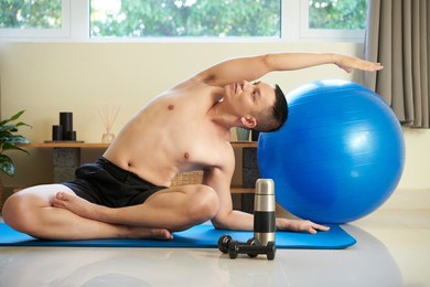 fit young man sitting in lotus position, raising arm and doing side bend