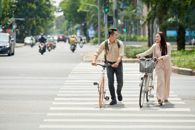 smiling young asian couple with bicycles crossing road on pedestrian crosswalk