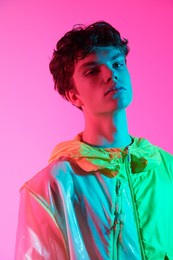 high fashion shot. portrait of a handsome male model with dark wavy hair posing in stylish designer jacket on a bright pink background. 