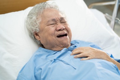 asian senior or elderly old lady woman patient feel pain in the chest and heart on bed in nursing hospital ward; healthy strong medical concept.
