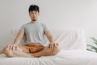 asian man do meditation on the sofa in his apartment. concept of wellbeing.