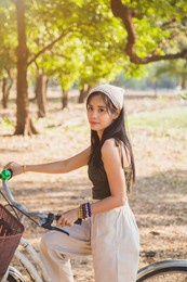 portrait asian woman in a green singlet sitting on a bicycle on a lawn with nature background in a park