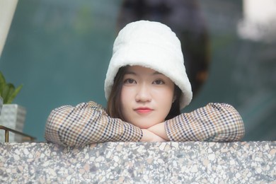 beautiful asian woman wears a white hat and plaid coat while she sitting near glassed window in new year and winter theme.