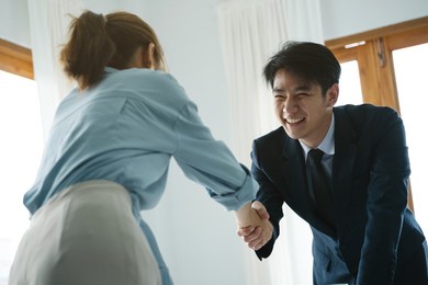 asian businessman and businesswoman shaking hands in office and smile, feeling happy.
