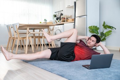 asian handsome active young man doing exercise on floor in living room. attractive male in sportswear spend leisure activity time to workout for health by follow online instruction on laptop at home.