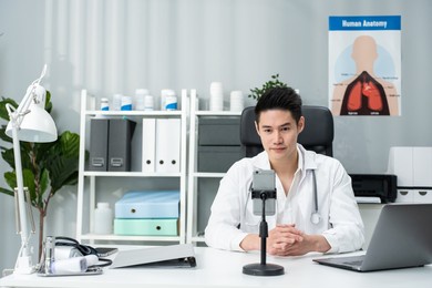 asian male medical doctor talking virtual online with patient at home. attractive physician man remote working from office hospital and broadcast diagnosis treatment to the sick people for telehealth.