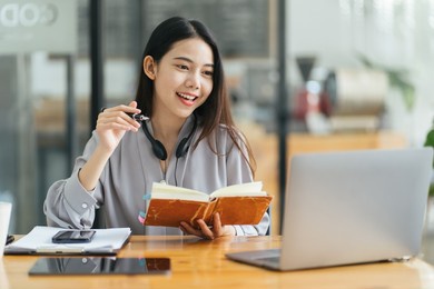 beautiful young freelancer woman using laptop computer sitting at cafe table. happy smiling girl working online or studying and learning while using notebook. freelance work, business people concept