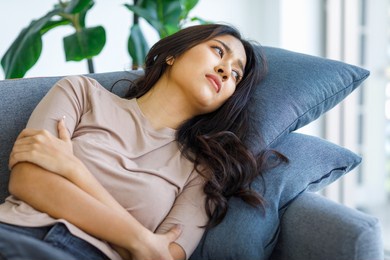 asian young stressed depressed thoughtful lonely sadness female model in casual outfit laying down crossed arms hugging herself alone on sofa in living room at home having depression sickness symptom.