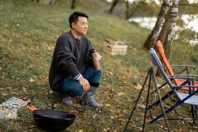 asian man resting while cooking and fishing on lake shore. concept of leisure, hobby and weekend in nature. autumn day