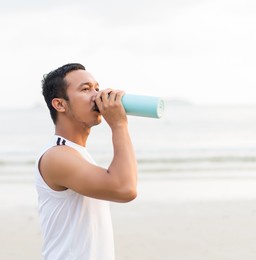 asian sport man drinking water while enjoying a morning run on the beach