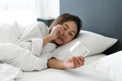 sleepy young asian woman lying in bed turning off an alarm clock in the morning