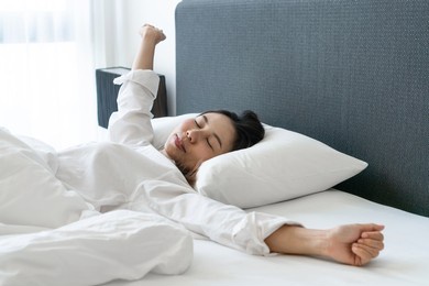 beautiful young asian woman in white pajamas stretching after wake up in the morning in bedroom at home. closeup