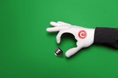 international intellectual property day. a hand in a white glove with a copyright sign, depicts a light bulb, with the outline of a human face. green background. the concept of copyright and ideas.