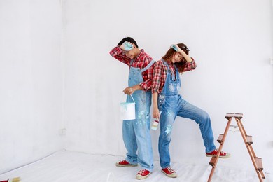 portrait of asian couple in plaid shirt with bear suit painting the interior white wall in new apartment concept,