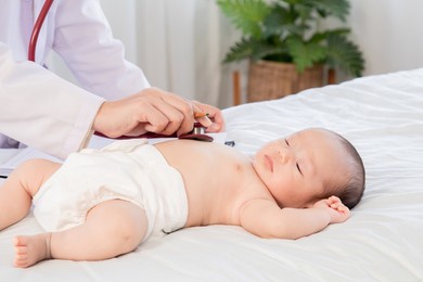 asian newborn baby get sick sleep during examine by pediatrician doctor hand hold stethoscope, little child in medicine hospital. physician hand using stethoscope examining adorable infant heart.
