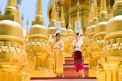 young woman with traditional burmese dress and carry bowl rice on her head  at beautiful golden pagoda in myanmar.