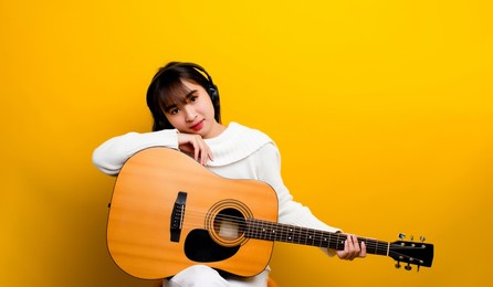 beautiful guitarist asian ethnic woman singing and playing guitar while sitting in a chair cross-legged. background color music and relaxation concepts