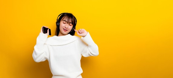 music listening to music beautiful asian woman in headphones listening to music and enjoying the sound of music. on a yellow background