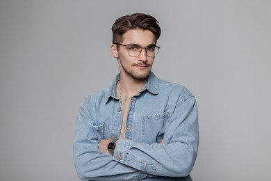 fashionable young handsome model hipster man with vintage eyewear with hairstyle in blue denim shirt in studio on a gray background