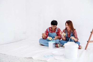 portrait of asian couple in plaid shirt with bear suit painting the interior white wall in new apartment concept,