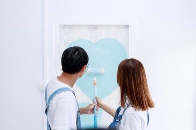 portrait of asian couple in plaid shirt with bear suit help painting the interior wall in new apartment concept,