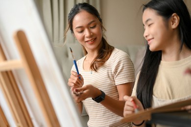 portrait of two asian sisters having a fun and happy time, painting and drawing on a canvas with water colour together.