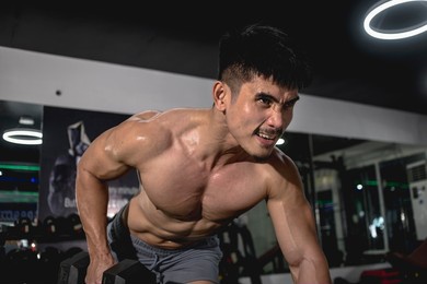 a serious and muscular asian guy grunts while doing one arm dumbbell rows on a bench, grimacing after feeling the lactic acid burn and near-failure. last set exercise. shirtless, vascular and ripped.